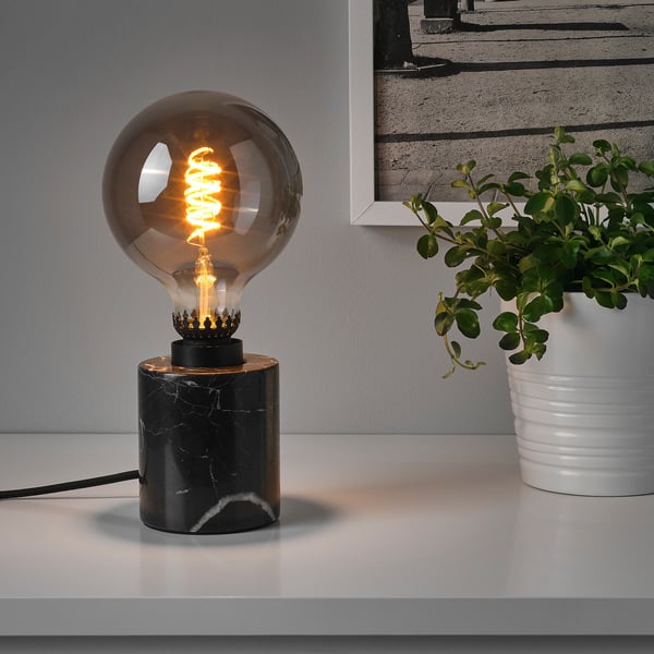 A table lamp with a black marble base and a glowing bulb atop, providing warm, mood lighting. The marble keeps the lamp stable.