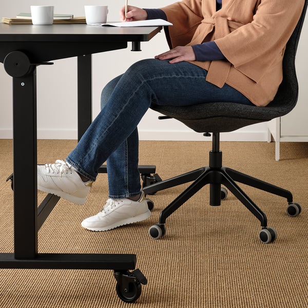Person sitting on ergonomic office chair, feet resting on adjustable footrest, writing at a height-adjustable desk.