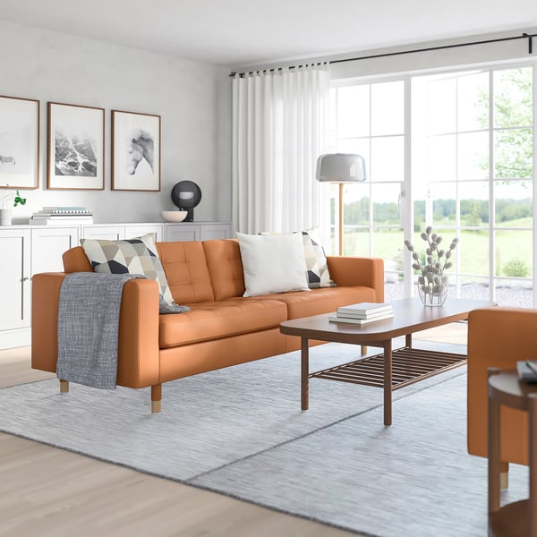 Cosy living room with large brown leather sofa, white curtains, wooden coffee table, and minimalist decor.