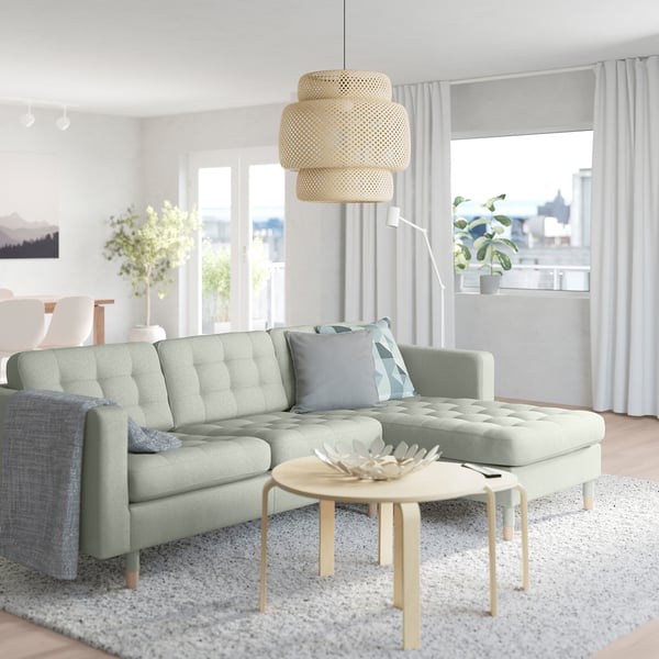 Modern living room with light green l-shaped sofa, wooden coffee table, and large window with city view.