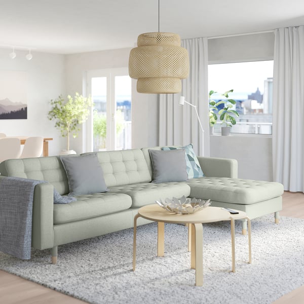 Modern living room with green MORABO sofa, wooden coffee table, large window, and warm decor.