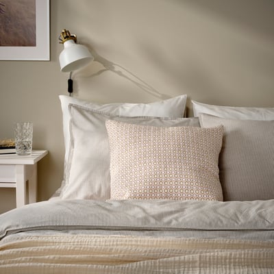 Bed with white & light pink MOROTSMOTT pillow, larger than glass, striped bedding, slight shadow from lamp.
