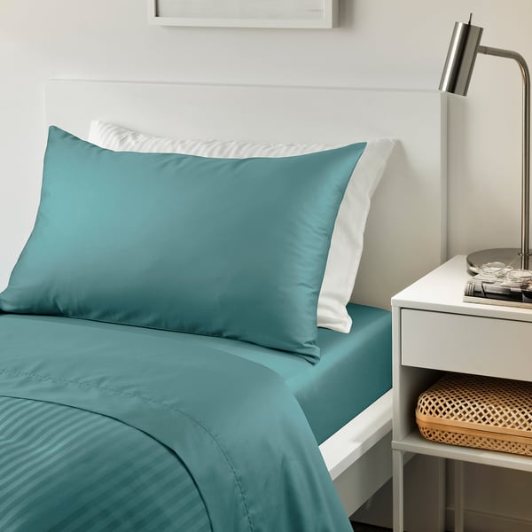 Bed with teal NATTJASMIN sheets, bedside table.