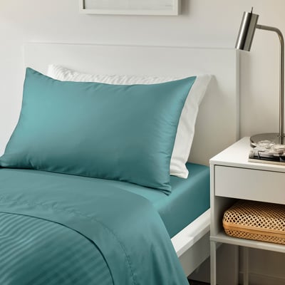 Bed with teal NATTJASMIN sheets, bedside table.