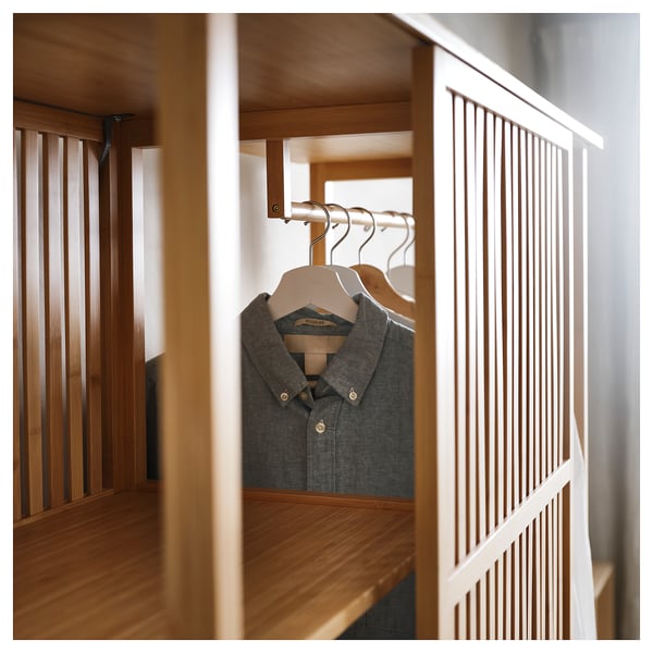 Scandinavian-style NORDKISA wardrobe in bamboo. Grey shirt hangs on a sliding door, dividing sides with open shelves.
