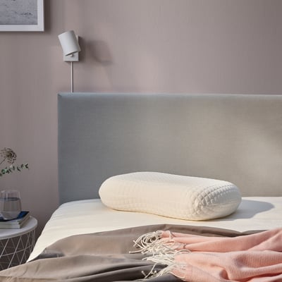 Bedroom with NORDSTÅLÖRT ergonomic pillow on a bed, side table with glass, books, scarf, wall light, and framed picture.