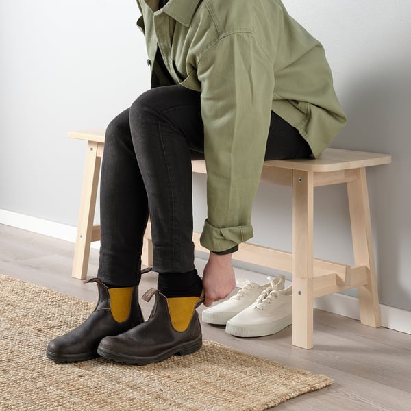 Two people sitting on wood online bench, one wearing black boots, the other white trainers.