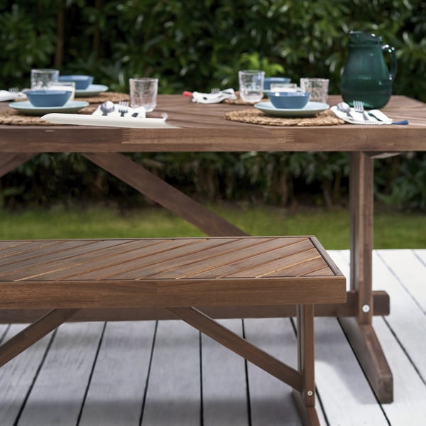 Outdoor dining table with herringbone pattern in brown acacia. Shown with plates, bowls, glasses. Rustic, sturdy design. Large size.
