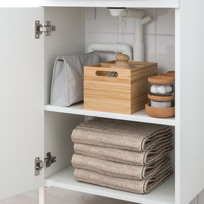 White bathroom cabinet with folded towels, wood box, and cork organiser.