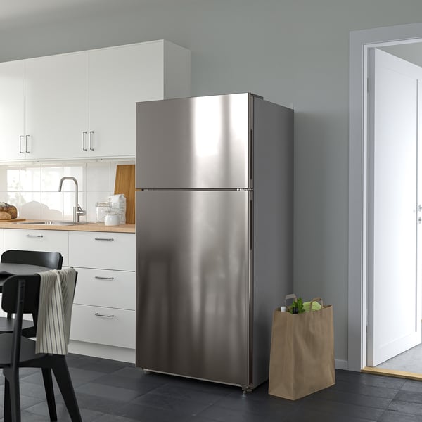 Stainless steel OLOFSFORS fridge in modern kitchen, taller than counter, beside brown paper bag with vegetables.