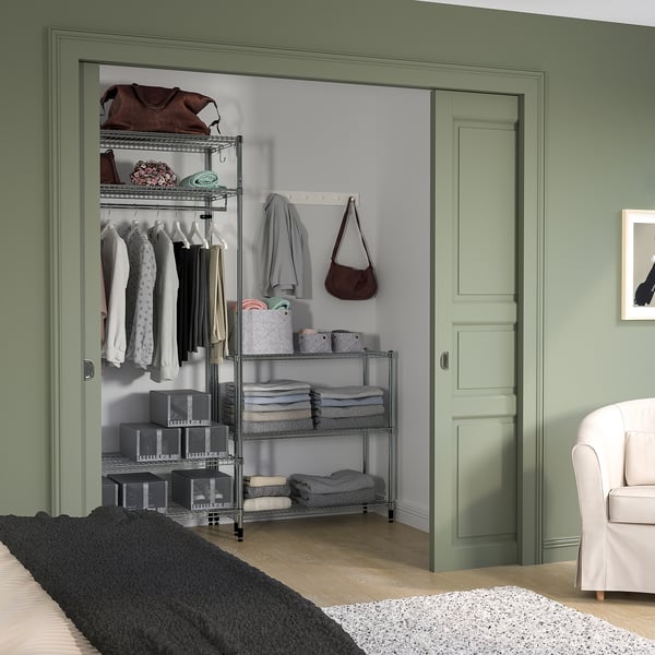 Green OMAR shelving with adjustable metal racks, neat clothes, and bags in a cosy green room.