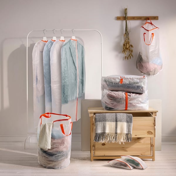 Blue PÄRKLA bags with orange handles, various sizes, some with blankets/clothes, around wooden chest and rack, fold flat when empty.