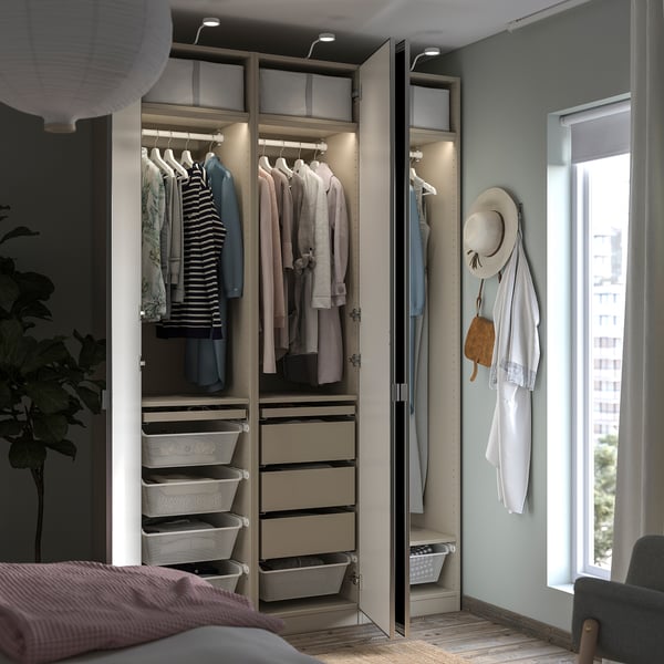 Modern bedroom with open PAX wardrobe, featuring clothes hangers, mesh baskets, and drawers. Soft lighting, mirror doors, and wooden floor.