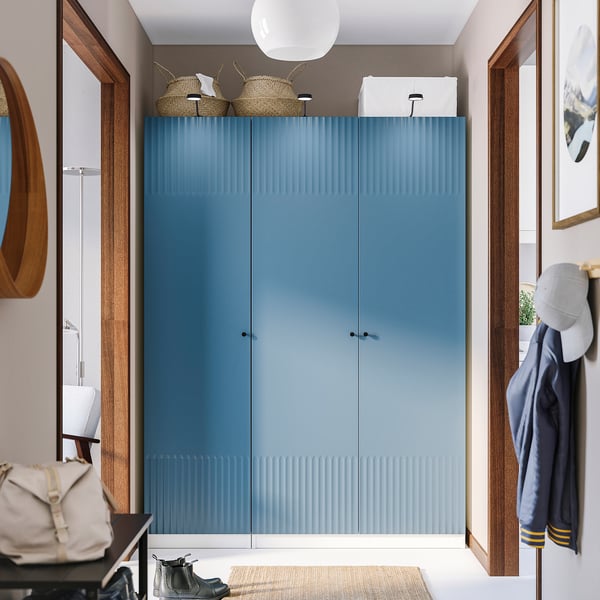 Modern blue PAX closet with door handles, fabrics, and a white rug, framed by wooden beams. Wardrobe taller than adjacent items.