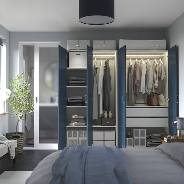 Modern bedroom with open blue PAX wardrobe, well-organized clothes and lighting, blue blanket on bed.