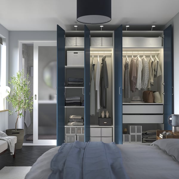 Modern bedroom with open wardrobe showing clothes, accessories, and lighting. Blue doors, shelves, and drawers visible.