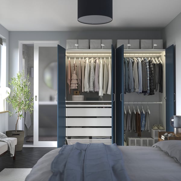 Modern bedroom with PAX wardrobe, hanging clothes, shelves, drawers, and soft lighting.