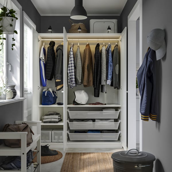 Open wardrobe with hanging jackets, folded clothes in drawers, helmet, bag, and cap.