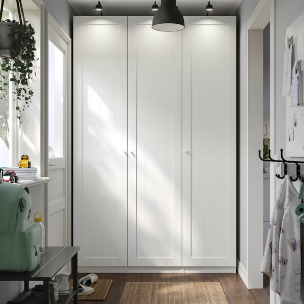 Dominating room, tall PAX wardrobe with table, books, plant. Black pendant light above, rug nearby.
