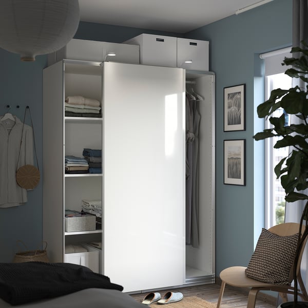 Bedroom with white wardrobe, blue walls, clothes, storage, plant, and sandals.