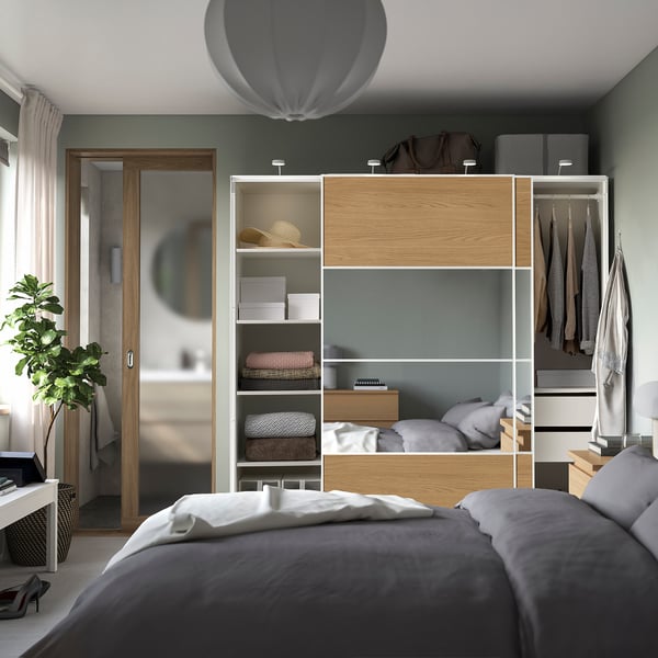 Modern bedroom a tall, wooden PAX wardrobe with sliding doors, multiple shelves, hanging space, and built-in lighting.