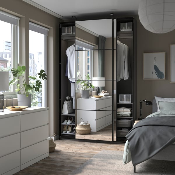Modern bedroom with PAX wardrobe in white, mirrored doors, grey bed, wooden floor, and paintings.