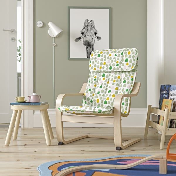Colourful kids POÄNG chair with green/yellow cushion on a rug, near teapot set and giraffe wall art.
