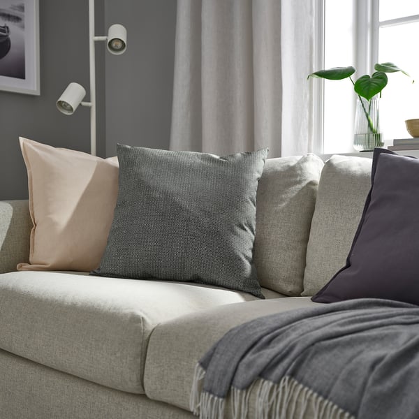 Modern neutral sofa with anthracite cushion, grey throw, plant, and tall windows.