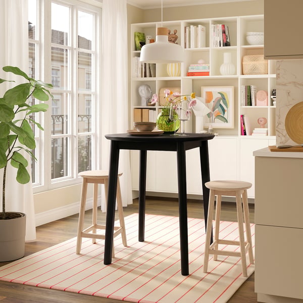 Black table, stools, striped rug, shelves, windows.