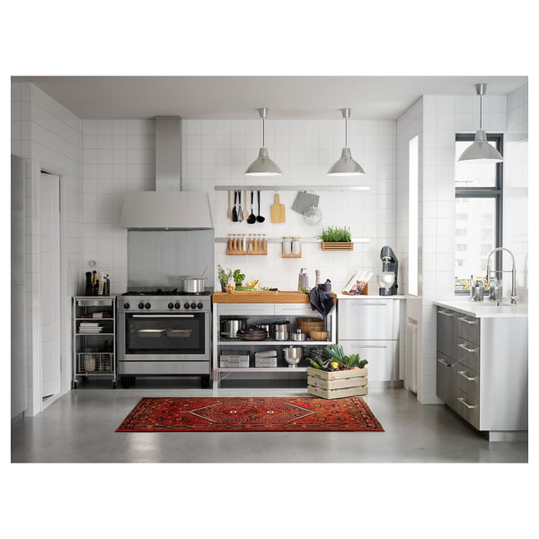 Modern kitchen with white cabinets, stainless steel appliances, bamboo-top island, hanging utensils, and red rug.