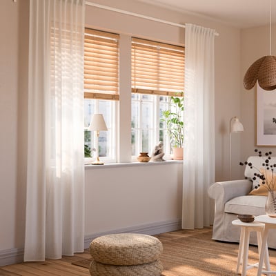 Comfortable living room with RITVA curtains, light pink, cotton, classic design, covering large window, complemented by cosy chair and lamp.