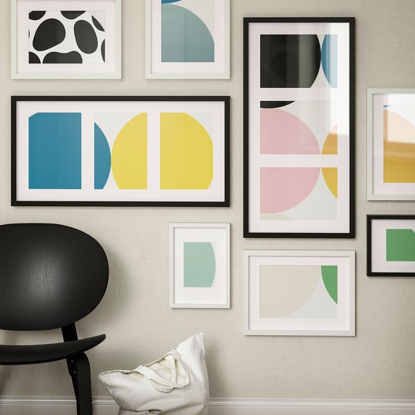 Colourful abstract art prints on a wall, with a yellow-blue large one, and a black chair with a white pillow.
