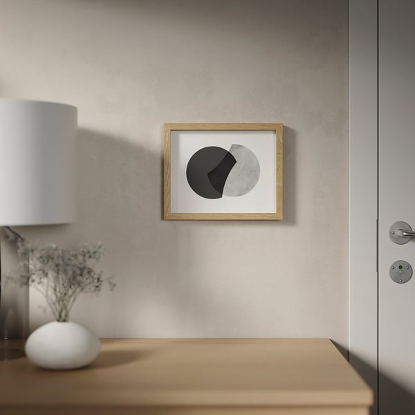 A minimalist art frame hangs on a textured wall above a wooden table with a lamp and vase.