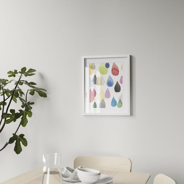 Framed, colourful droplet art hung above a dining table with a plant and place settings, displaying versatile decor.