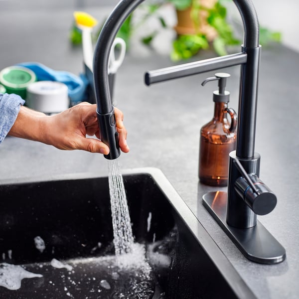 Person operates modern kitchen tap with pull-down spray, showcasing its dual spray functionality and high-arc design.