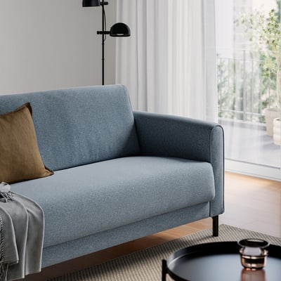 A light blue sofa with black accents, a pillow, and blanket in a bright, minimalist living room.