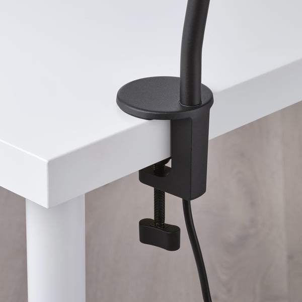 Black desk lamp securely clamped to a white desk edge, showcasing robust build and adjustable arm, efficiently designed for workspace illumination.