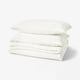 Stack of white SCHERSMIN cotton bed linens, including pillows and folded sheet. Soft, organic, wavy texture.