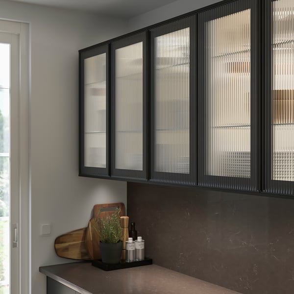Modern kitchen with black SEKTION cabinets, sleek reeded glass doors, and brown countertop. Small plant and bottles sit on counter.