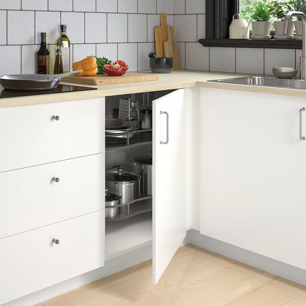 Modern kitchen with organised corner cabinet, wooden counter, fresh veggies, grey backsplash, stainless sink.