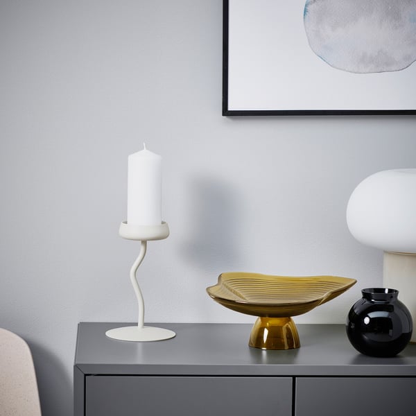 Modern decor: white SILVERPÄRON candlestick, sleek & slender, stands tall next to golden bowl & black vase on grey console.