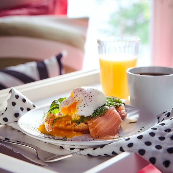 Breakfast on pink tray: orange juice, coffee, and salmon with poached egg on bread.