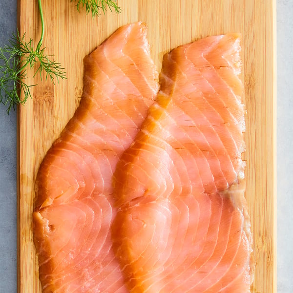 Raw salmon fillets on wooden board, light pink with fatty lines, garnished with fresh green dill.