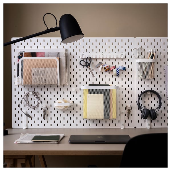 SKÅDIS white pegboard with accessories: lamp, scissors, headphones, mesh organisers. Organised home office setup.