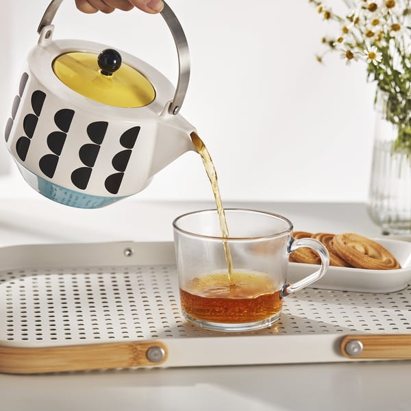 Teapot pouring tea into cup, with removable infuser and foldable handle.