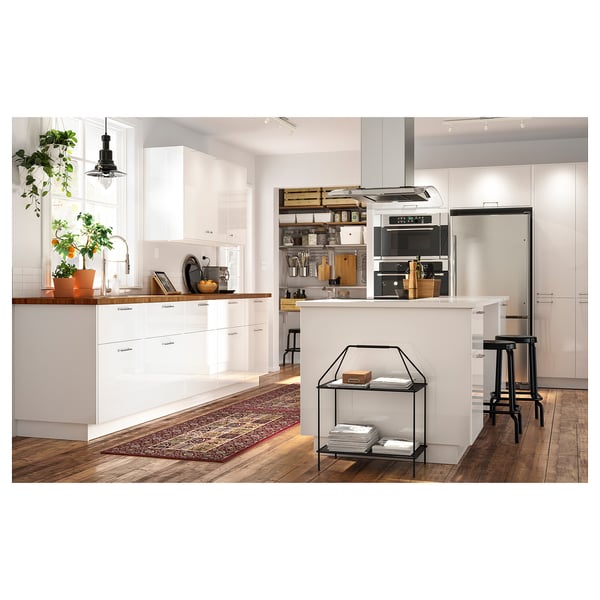 Modern white kitchen with a wooden island, stainless steel appliances, black bar stools, hanging plants, and a red rug.