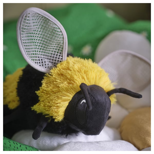 A SKOGSDUVA bee toy, black and yellow, soft and plush, designed to hang. Its smaller than the nearby items, made from recycled polyester.