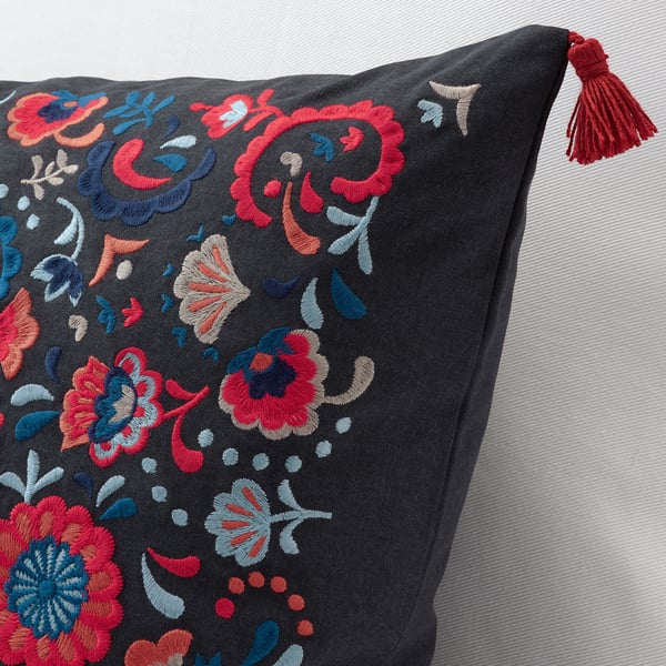 Embroidered cushion with vibrant floral patterns and red tassels on dark fabric. Intricate stitching high-quality craftsmanship.
