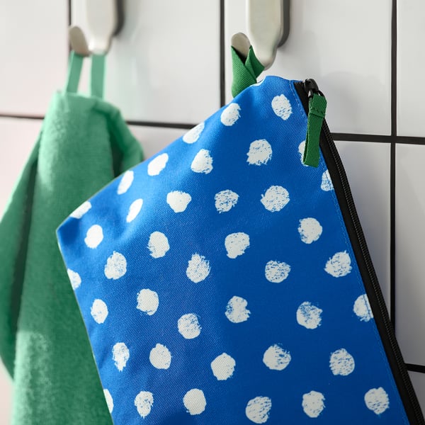 Blue toiletry bag with white polka dots hangs from a hook, featuring a green zip and compartments for organisation.