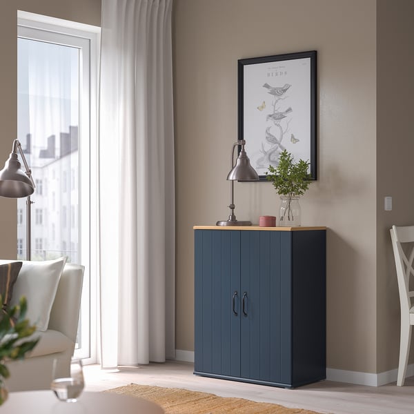 Grey SKRUVBY cabinet in corner, near window and chair, topped with lamp, candle, and vase.